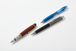 Wooden fountain pen, blue ballpoint pen, and black rollerball pen on a white background.