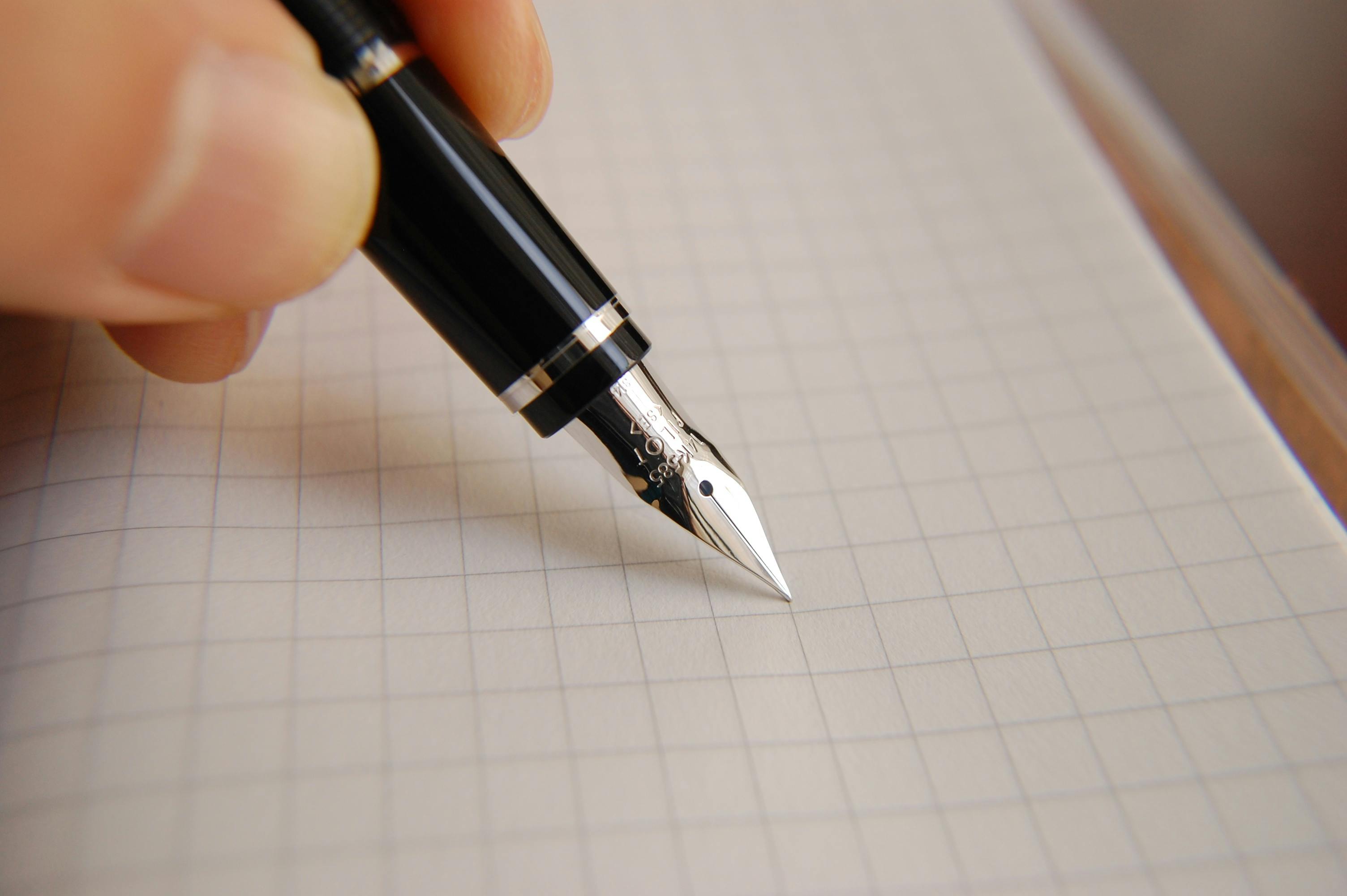 Hand writing with a black and silver fountain pen on grid paper notebook.